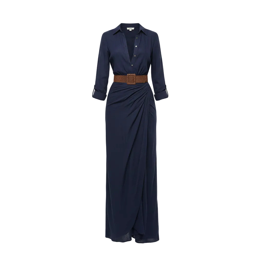 Woman wearing a long navy dress with a brown belt and holding a woven bag against a plain background