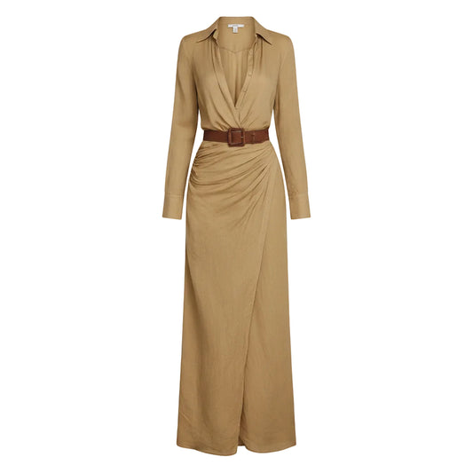 Woman wearing a long beige dress with a belt, holding a woven bag against a plain background.