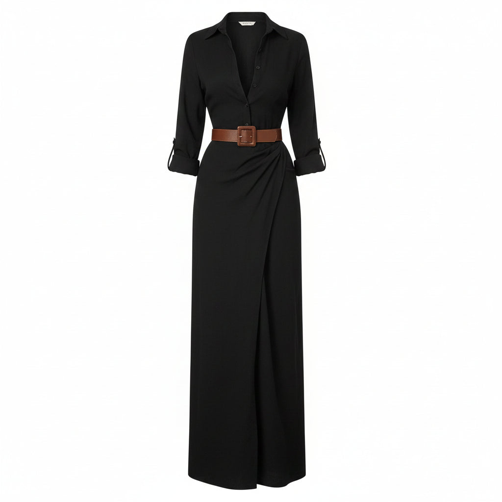 A woman models a long black button-front shirt dress with a deep V-neck, long sleeves, and a matching long skirt. She wears a brown belt with a large square buckle at the waist and carries a woven straw tote bag against a textured light gray wall.