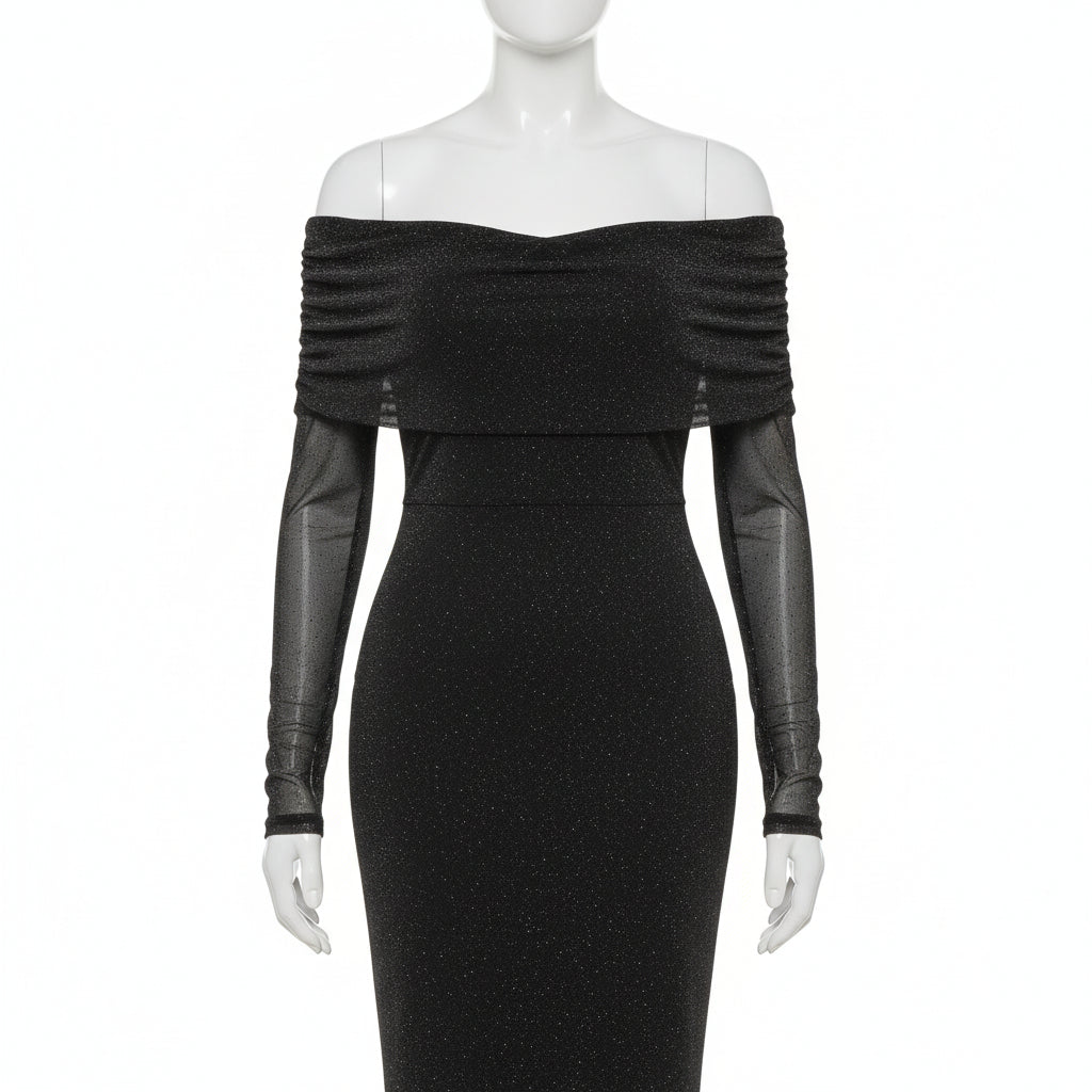Woman wearing a black off-shoulder dress with sheer sleeves against a white wall.
