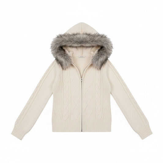A woman wearing a cream cable-knit zip-up hoodie with a gray faux-fur trimmed hood, paired with blue jeans, in a bedroom setting.